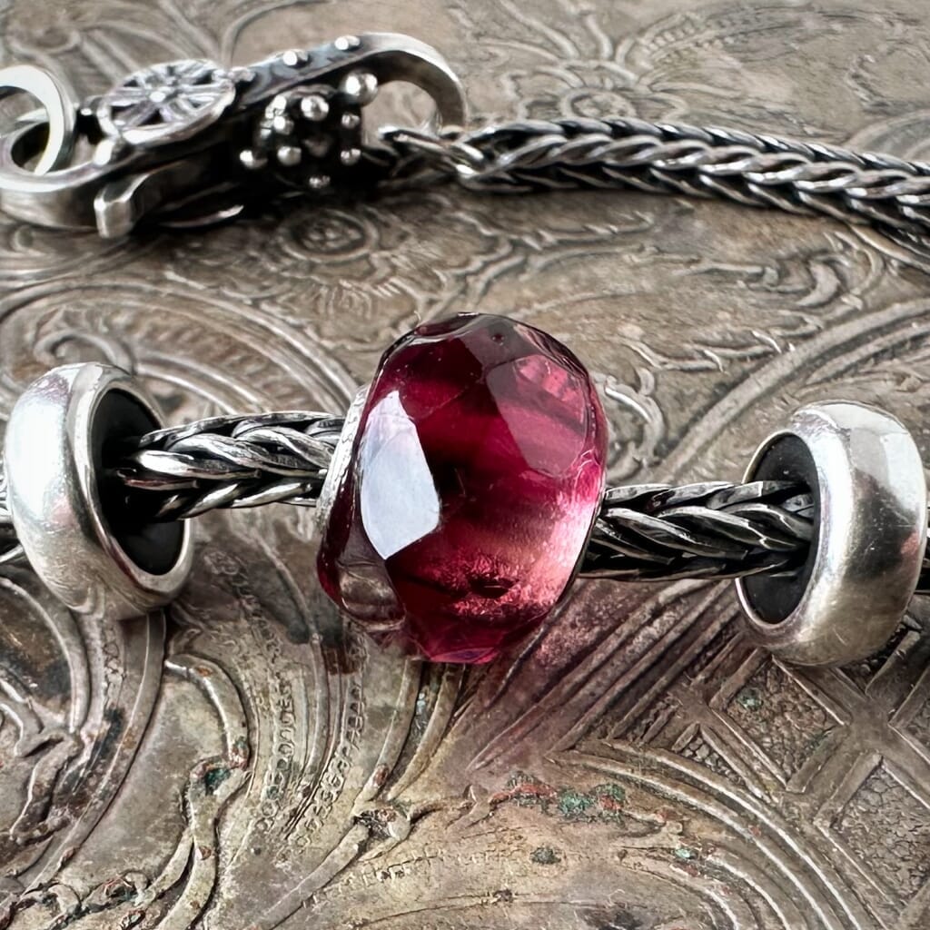 Trollbeads RED PINK PRISM glass bead, looks like a juicy pomegranate seed, shown on a silver Trollbeads bracelet, with two spacers and lock.