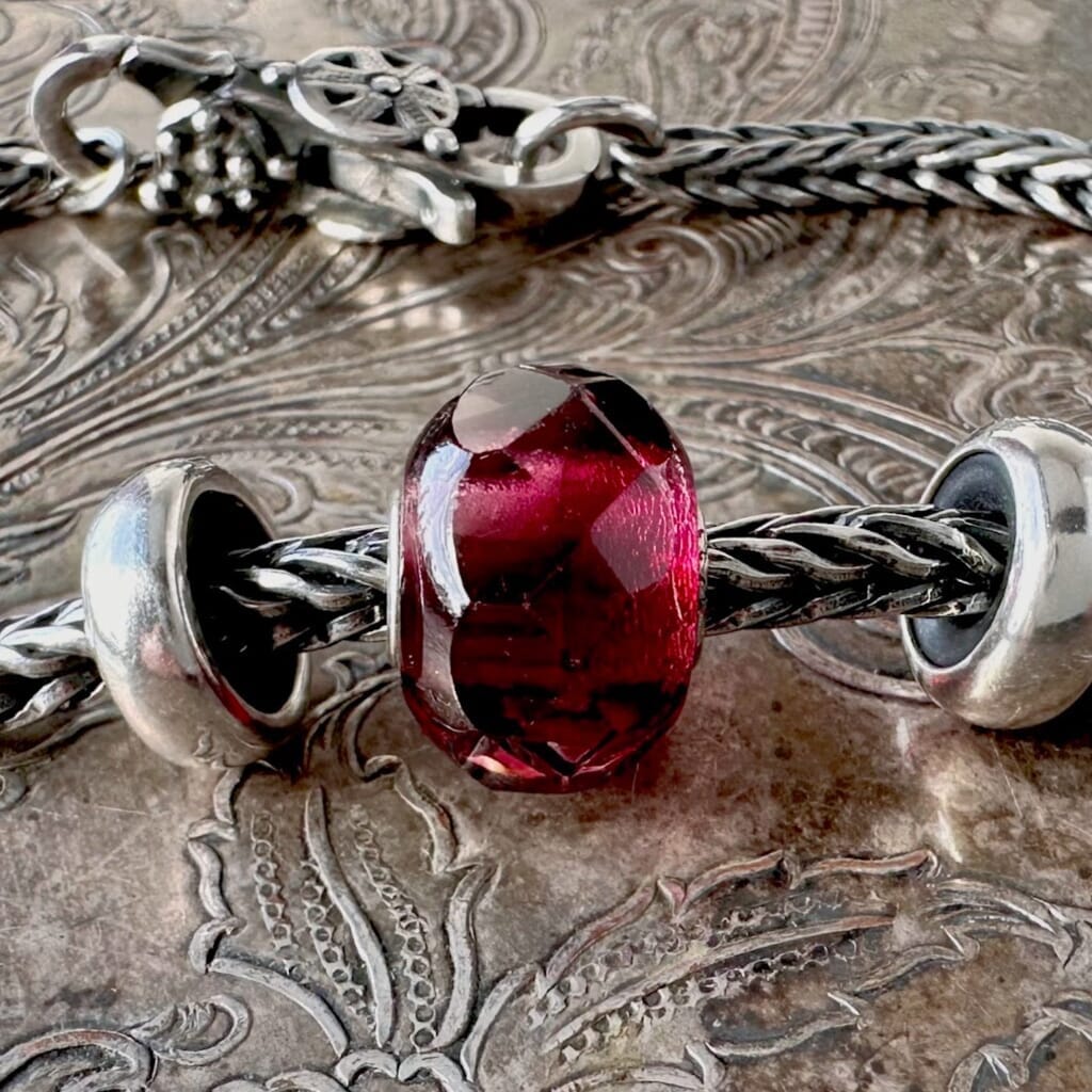 Trollbeads RED PINK PRISM glass bead, looks like a juicy pomegranate seed, shown on a silver Trollbeads bracelet, with two spacers and lock.