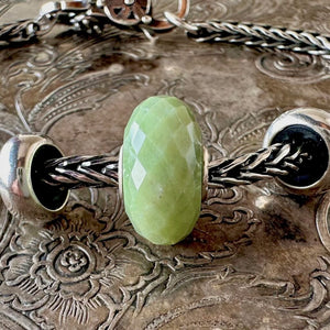 Trollbeads SERPENTINE faceted, gemstone bead is a calming, opaque green colour, and is shown on a Trollbeads silver bracelet.