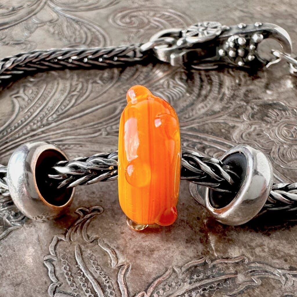 Trollbeads STRIPED BUD is a yellow-orange glass bead with a mix of whimsical stripes and clear dots, shown on a Trollbeads silver bracelet.