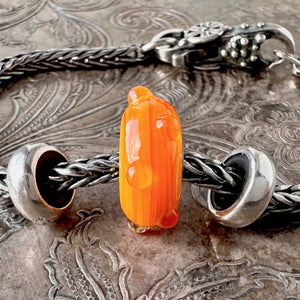 Trollbeads STRIPED BUD is a yellow-orange glass bead with a mix of whimsical stripes and clear dots, shown on a Trollbeads silver bracelet.